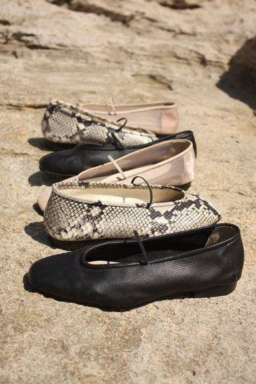 Deia ballet flats in snake print, black leather and nude lined up on a sunlit rock