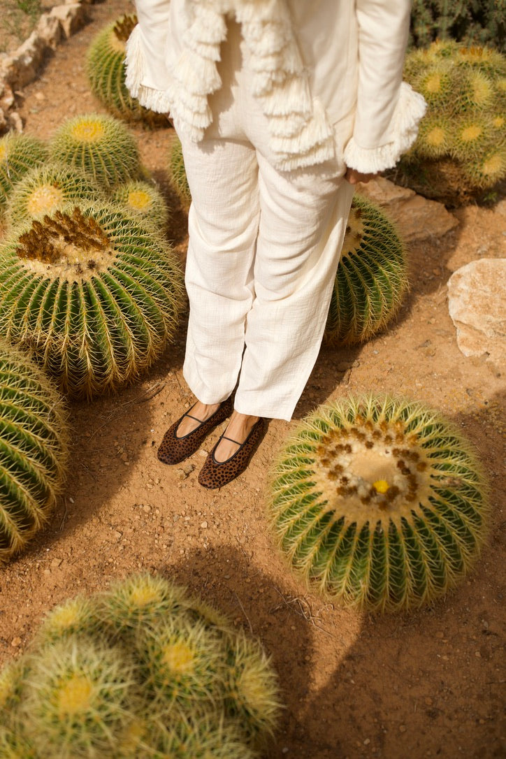 Cheetah-print Deia ballet flats worn with white trousers among golden barrel cacti