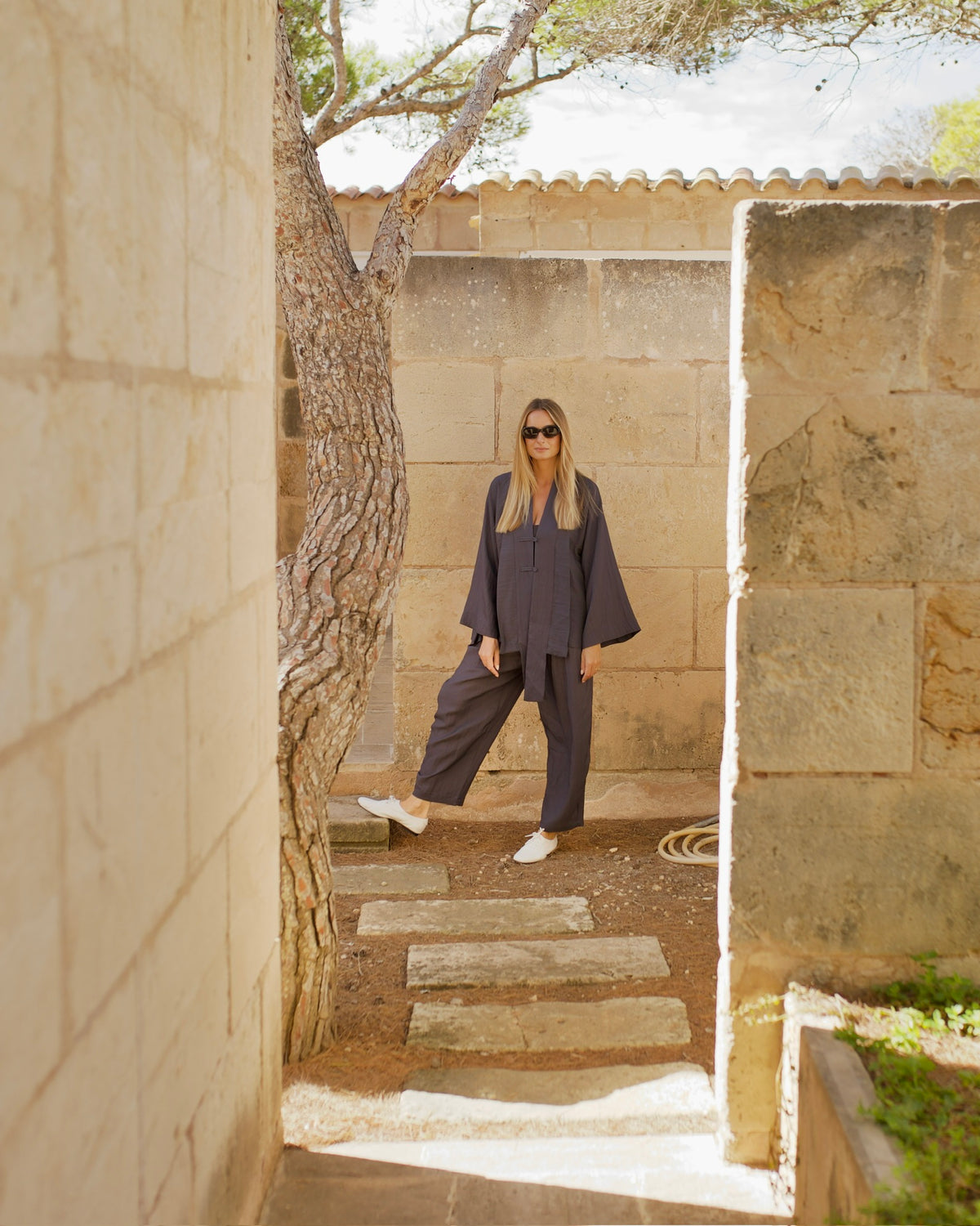 Woman in a charcoal linen set in a stone courtyard, wearing white leather Inca Oxfords