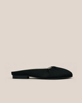 A single black satin mule flat shoe with a low block heel, shown in profile against a solid light beige background.